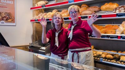 Zwei Verkäuferinnen stehend winkend vor Theke einer Bäckerei