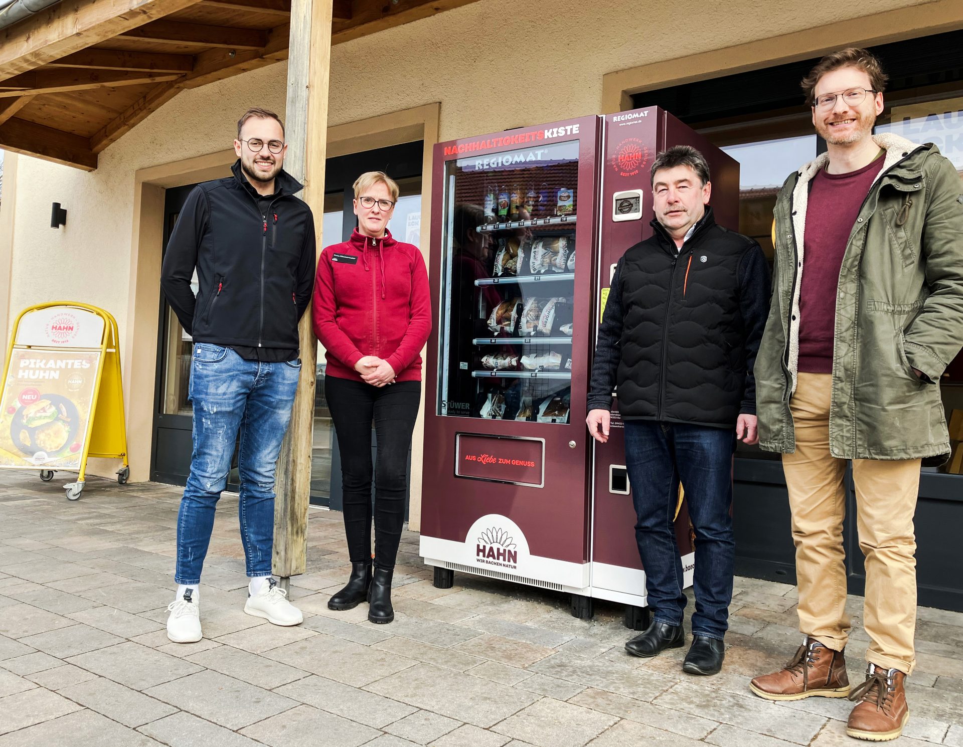 Vier Personen stehen vor dem Verkaufsautomaten der Bäckerei Hahn.